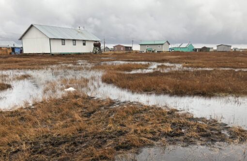 Photo of thawing permafrost, water, and white and green homes in Alaska.