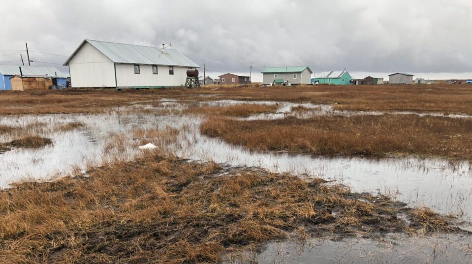 Photo of thawing permafrost, water, and white and green homes in Alaska.