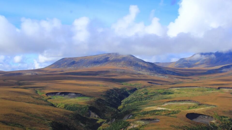 photo of green and brown tundra under blue sky with clouds at Peel Plateau, Northwest Territories, Canada